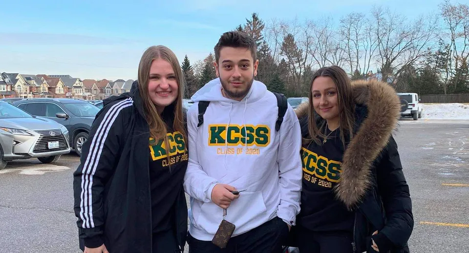 Tre studenti si trovano insieme nell'area esterna della King City Secondary School con case d'abitazione sullo sfondo.