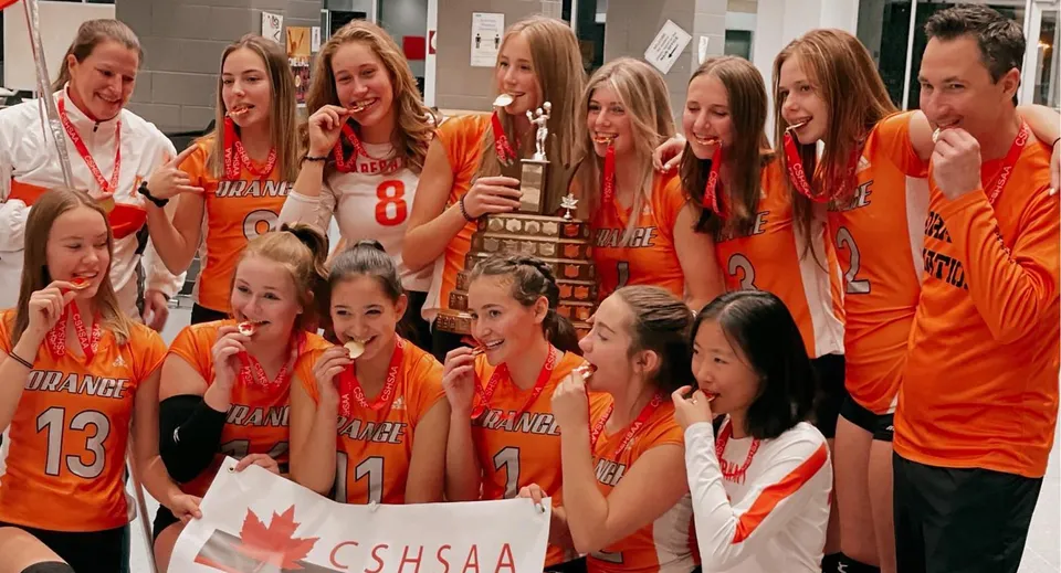 Un gruppo di giovani atlete posa insieme nell'area della Bowness High School con la bandiera canadese sullo sfondo.