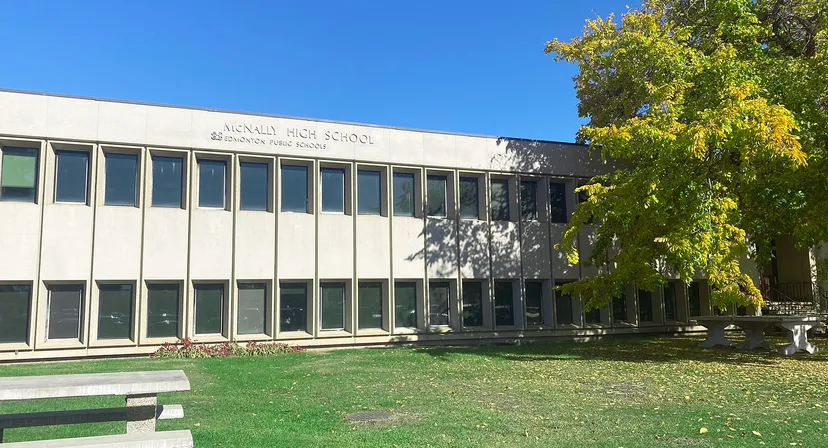L'edificio moderno a più piani della McNally High School è circondato da una verde vegetazione sotto un cielo blu.