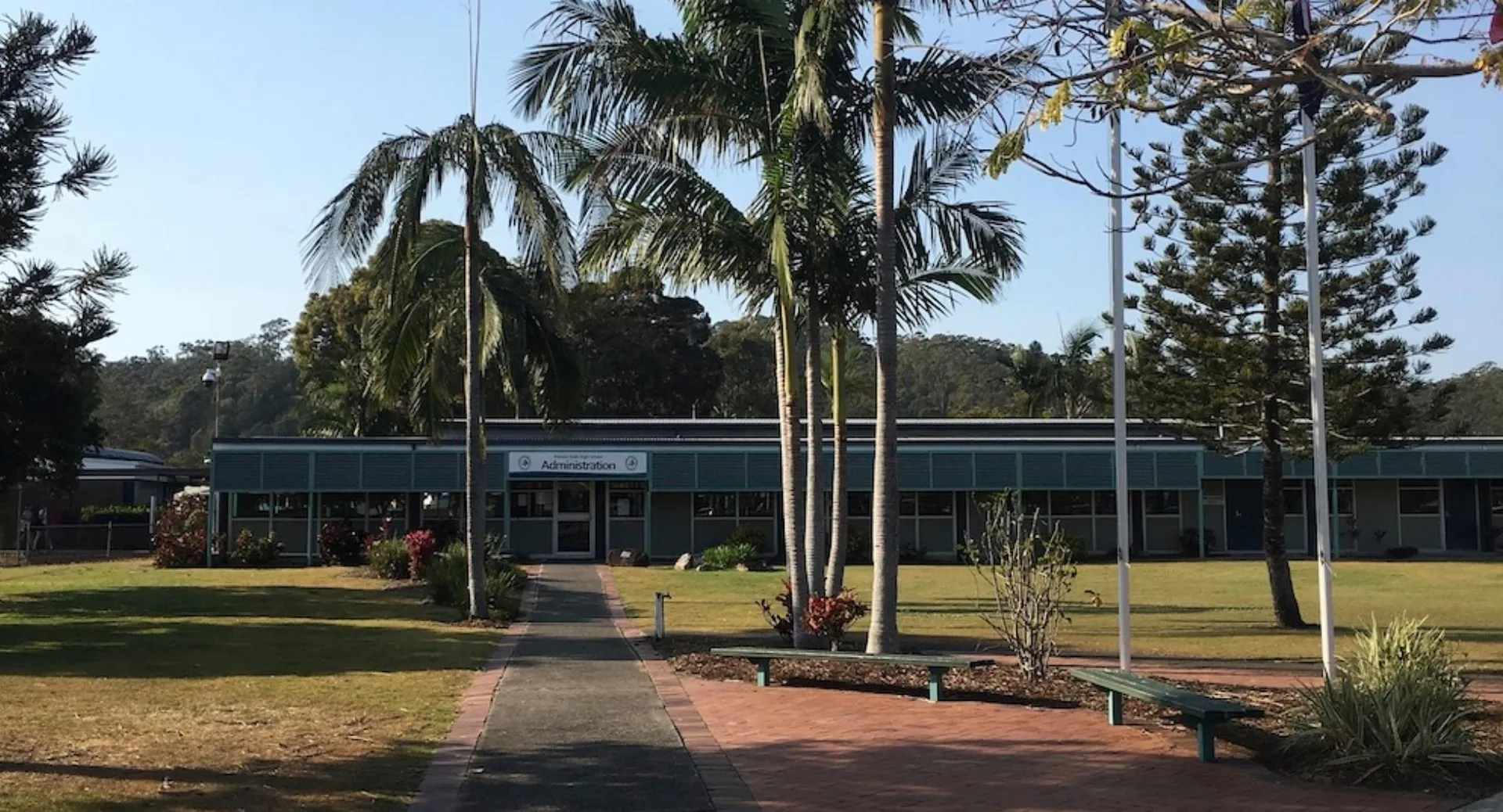 L'edificio a un piano con il tetto verde della Elanora State High School è circondato da palme e aree verdi.