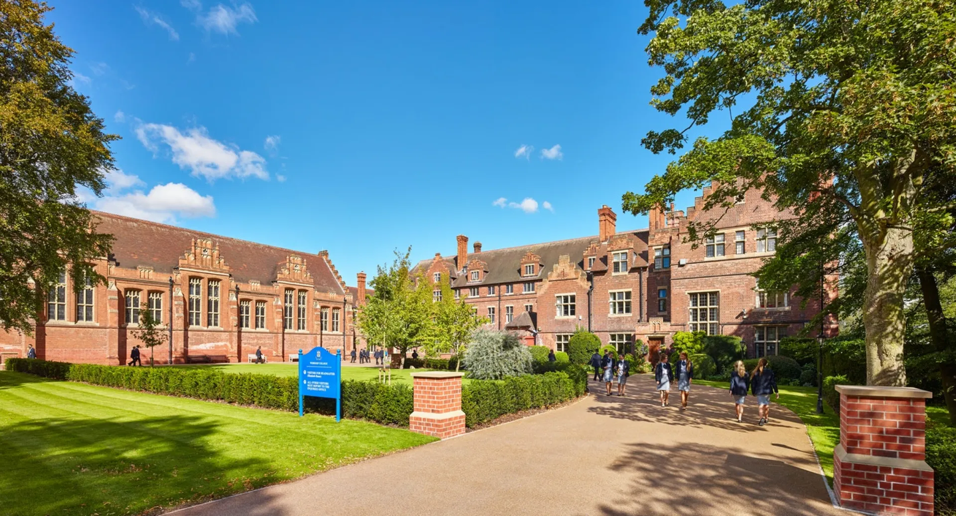 Il campus del Worksop College mostra un viale lastricato attraverso un prato verde circondato da edifici in mattoni sotto un cielo blu.