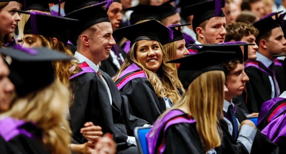 Neodiplomati e neodiplomate del Portsmouth College in abiti accademici colorati si riuniscono per festeggiare.