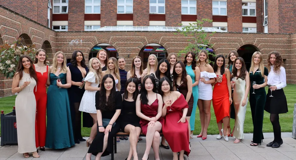 Un gruppo di giovani donne in abito formale è in piedi davanti a un edificio in mattoni con finestre ad arco nel campus della Badminton School.