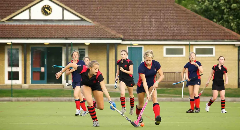Un gruppo di studentesse della Stamford Endowed Schools gioca a hockey su prato su un campo in erba davanti a un edificio tradizionale.