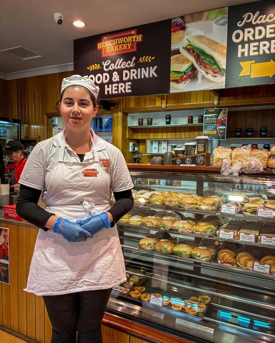 Una studentessa del Cathedral College Wangaratta indossa un grembiule e sta davanti al banco di una panetteria.