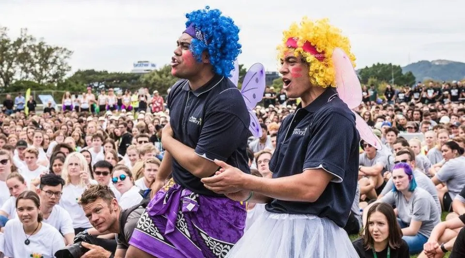 Due persone con i capelli colorati sono in piedi davanti a una grande folla nel campus della Victoria University of Wellington.