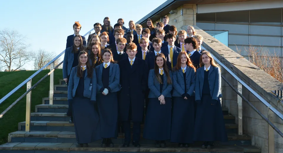 Un gruppo di studenti della Uppingham School è sulle scale davanti a un edificio con facciata in vetro.