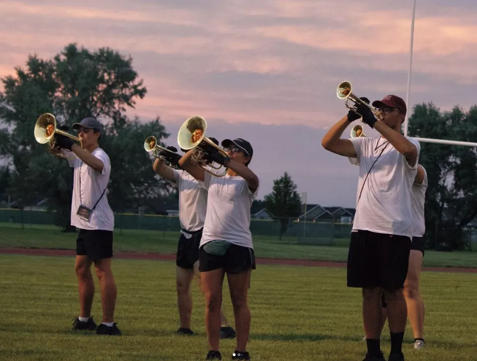 Un gruppo di studenti della Bonneville High School suona le trombe all'aperto davanti a un campo erboso e a un cielo serale colorato.