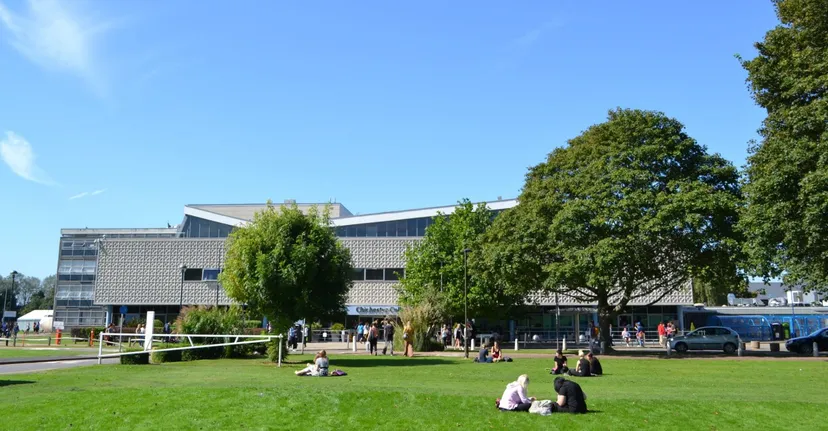 Persone sedute su un prato davanti a un edificio moderno nel campus del Chichester College.
