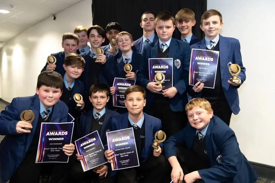 Un gruppo di studenti del St. John Plessington Catholic College posa nel corridoio con vari premi e trofei.