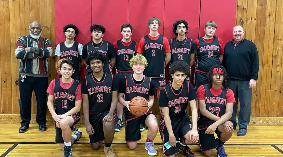 Un gruppo di studenti e studentesse della Harmony Christian School posa insieme nella palestra durante una partita di basket.