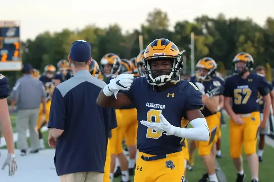Un giocatore di football americano della Clarkston High School in divisa blu e gialla sul campo.