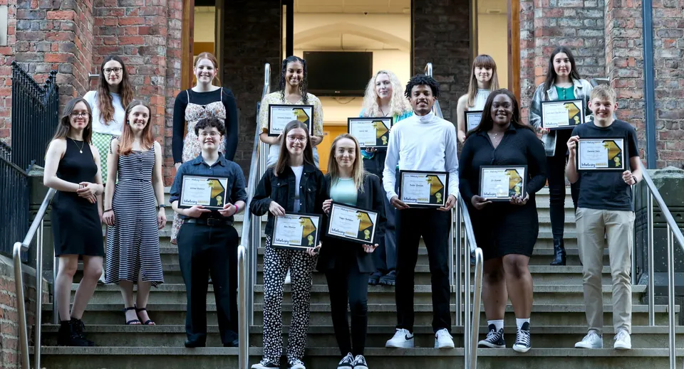 Studenti del Queen Elizabeth’s 6th Form con certificati davanti a un edificio in mattoni.