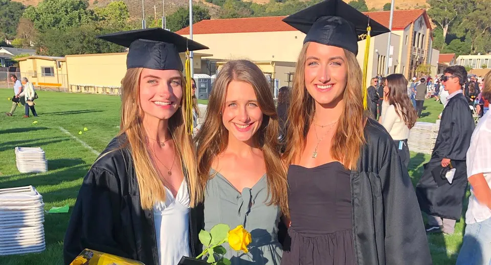 Tre studentesse con cappelli e tocchi di laurea sono in piedi insieme davanti a un prato nel campus del San Luis Coastal Unified School District.