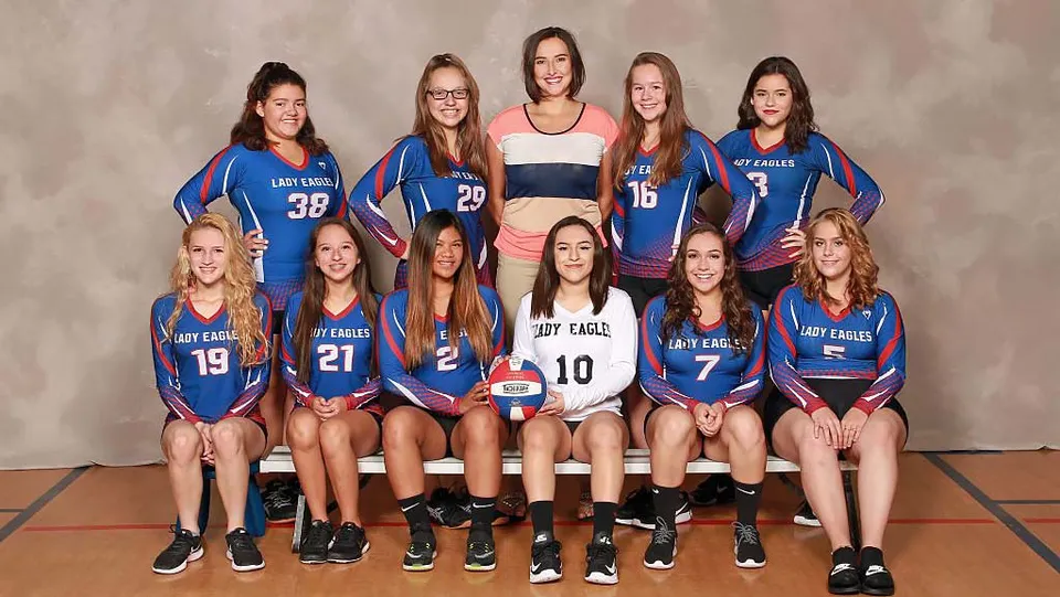 Un gruppo di giovani giocatrici di pallavolo della Evangel Christian Academy posa in divise blu e bianche in uno studio.