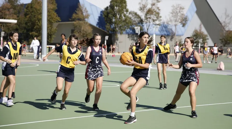 Studentesse dell'Ashdale Secondary College giocano a basket su un campo all'aperto, circondate da alberi ed edifici.