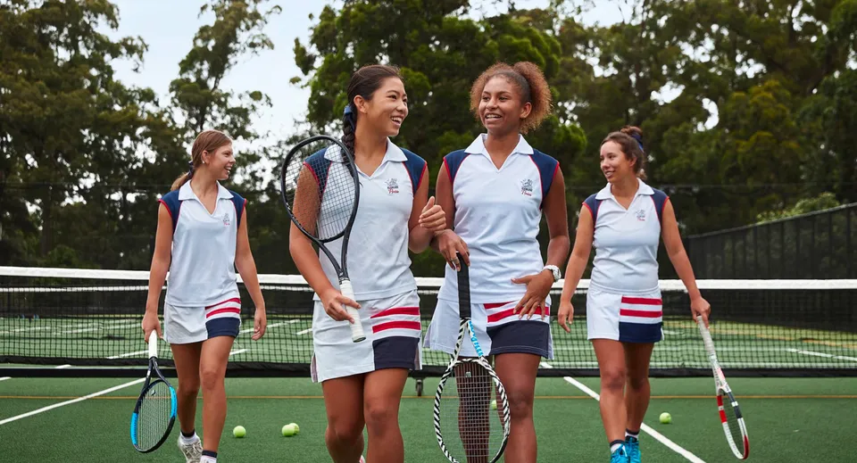 Un gruppo di giovani tenniste si trova sul campo da tennis del Pymble Ladies College circondato da alberi e aree verdi.