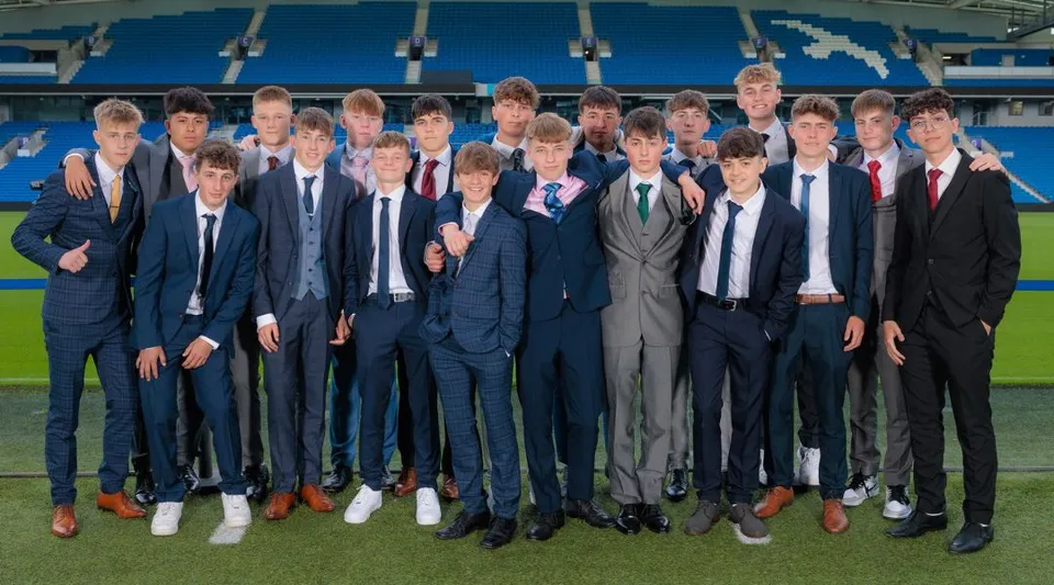 Un gruppo di giovani uomini in abito formale si trova sul campo sportivo della Steyning Grammar School and Sixth Form con un grande stadio sullo sfondo.