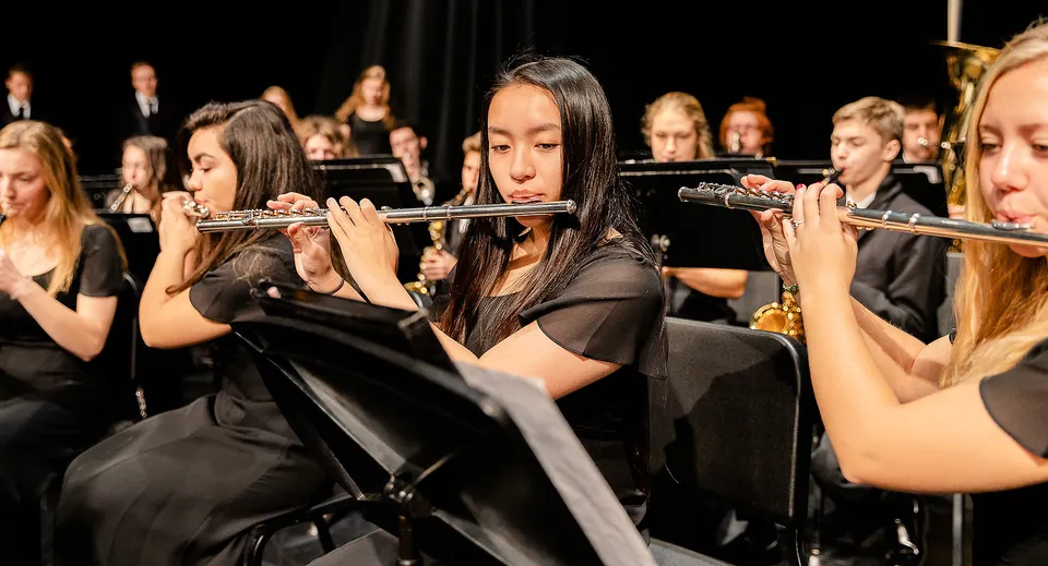 Studenti della Holland Christian Schools suonano strumenti a fiato su un palco con sfondo scuro.