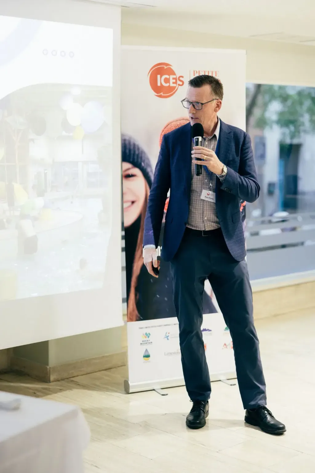 Ponente con micrófono hablando junto a un roll up de ICES en un evento informativo
