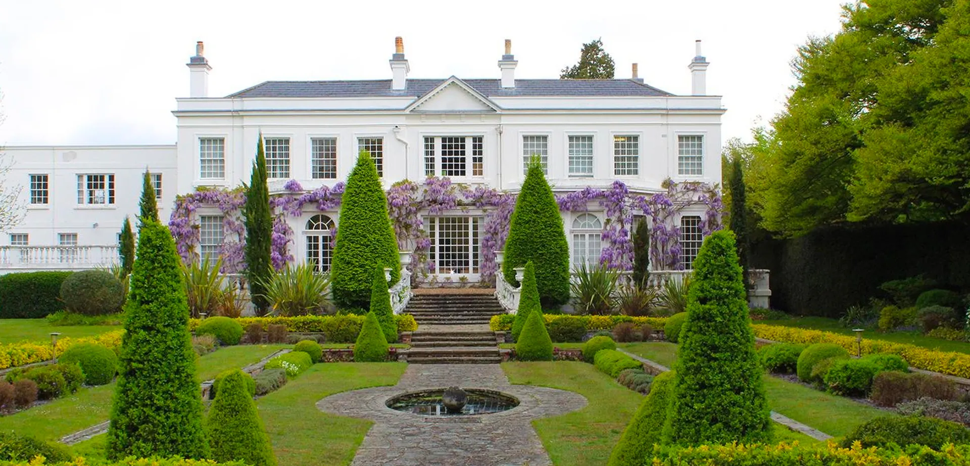 La villa bianca con facciata simmetrica e un glicine in fiore nel giardino della ACS International School Cobham.