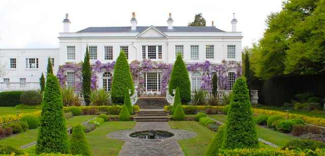 La villa bianca con facciata simmetrica e un glicine in fiore nel giardino della ACS International School Cobham.