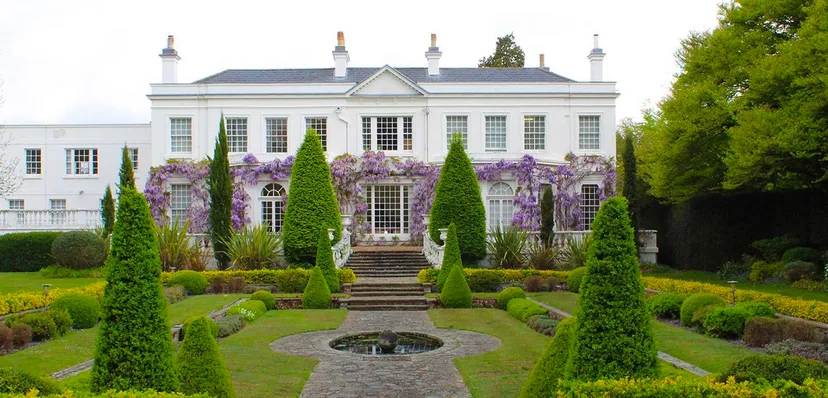 La villa bianca con facciata simmetrica e un glicine in fiore nel giardino della ACS International School Cobham.