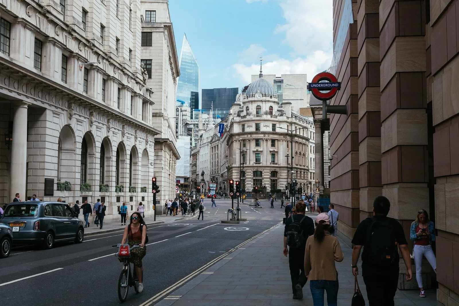Belebte Londoner Straße mit Radfahrerin, schwarzem Taxi und Underground-Schild