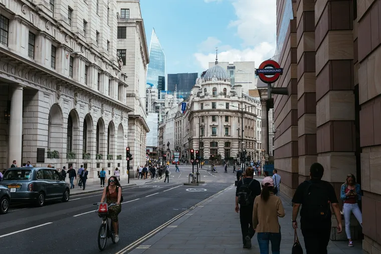 Belebte Londoner Straße mit Radfahrerin, schwarzem Taxi und Underground-Schild