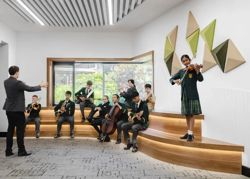 Gli studenti della Macarthur Anglican School suonano vari strumenti musicali sotto la direzione di un insegnante in un'aula moderna.