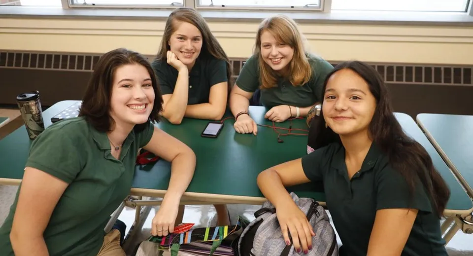 Quattro studentesse della Rice Memorial High School siedono insieme in classe e sorridono alla telecamera.