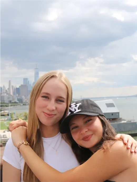 Due ragazze sorridenti abbracciate con lo skyline di New York sullo sfondo