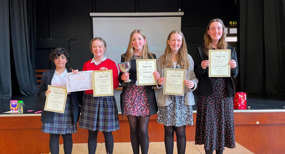 Un gruppo di giovani studentesse della Rye St. Antony School tiene in mano certificati e premi davanti a un palcoscenico.