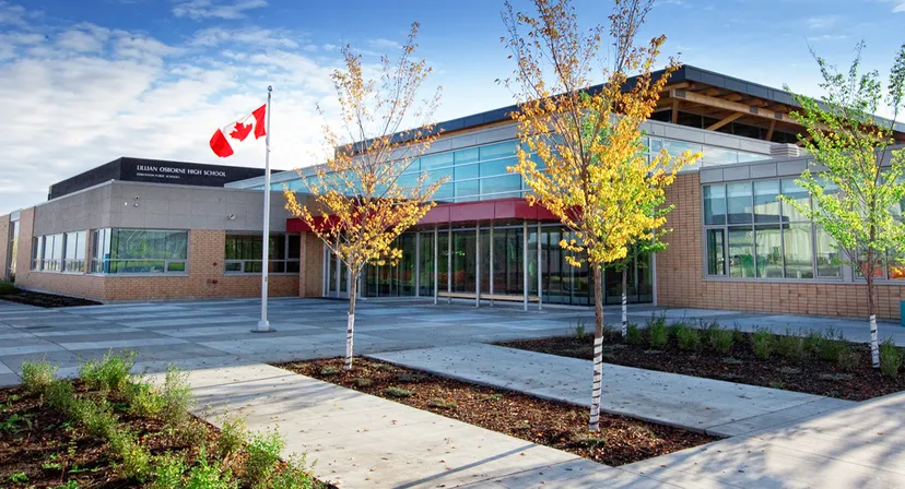 L'edificio moderno della Lillian Osborne High School con la bandiera canadese e alberi dai colori autunnali nei dintorni.