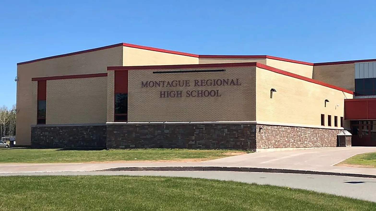 El moderno edificio de varias plantas con tejado de tejas rojas de la Montague Regional High School se encuentra sobre un césped bajo un cielo despejado.