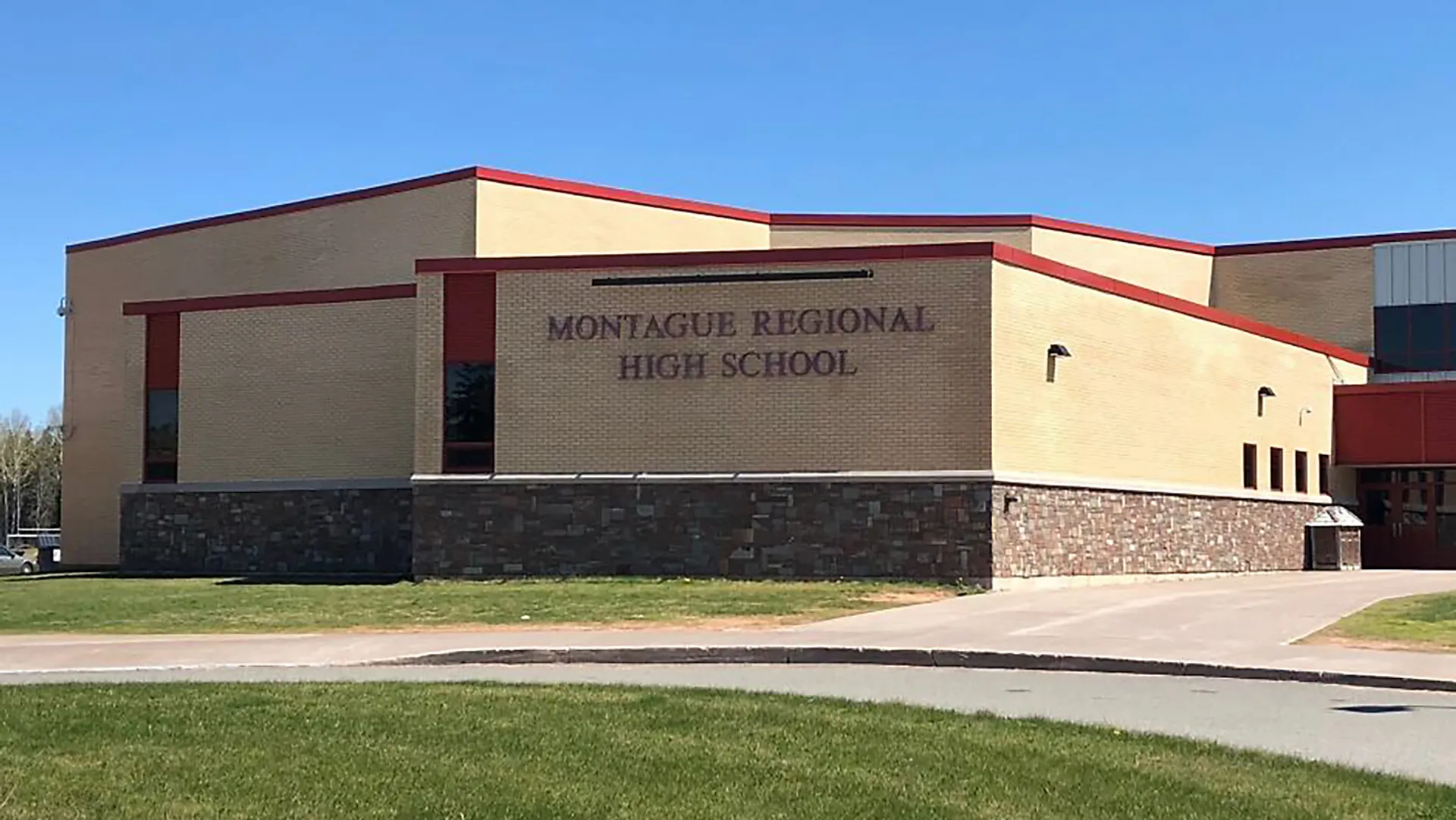 L'edificio moderno a più piani con tetto in tegole rosse della Montague Regional High School sorge su un prato sotto un cielo limpido.
