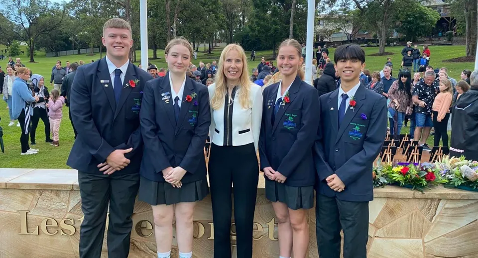 Un gruppo di studenti della Helensvale State High School in abiti formali è in piedi davanti a una struttura in pietra all'aperto.
