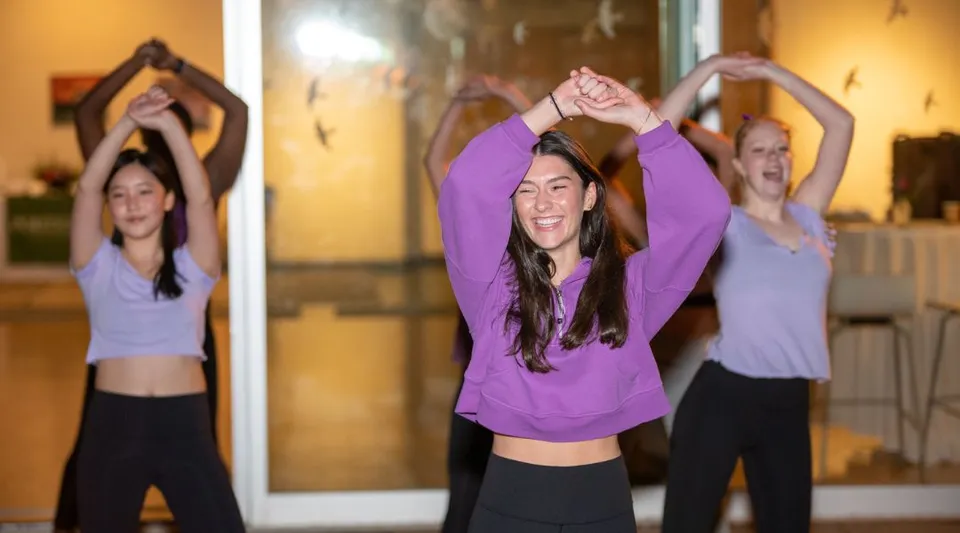 Tre studentesse della Miss Porter's School eseguono esercizi di yoga con le braccia alzate in uno studio.