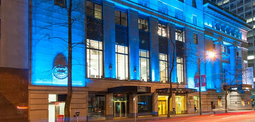 L'edificio a più piani della Alexander Academy è visibile di notte con le finestre illuminate e gli alberi di fronte.