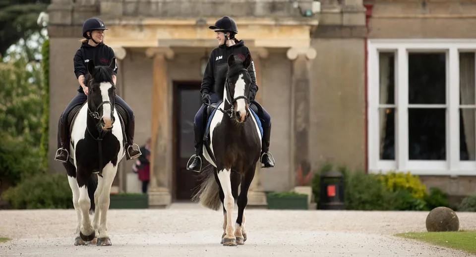 Due cavalieri in abbigliamento da equitazione davanti a un edificio storico nel campus della Queen Margaret’s School.