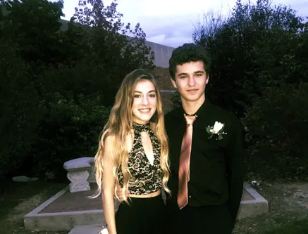 Un chico con camisa negra y corbata posa junto a una chica vestida de gala