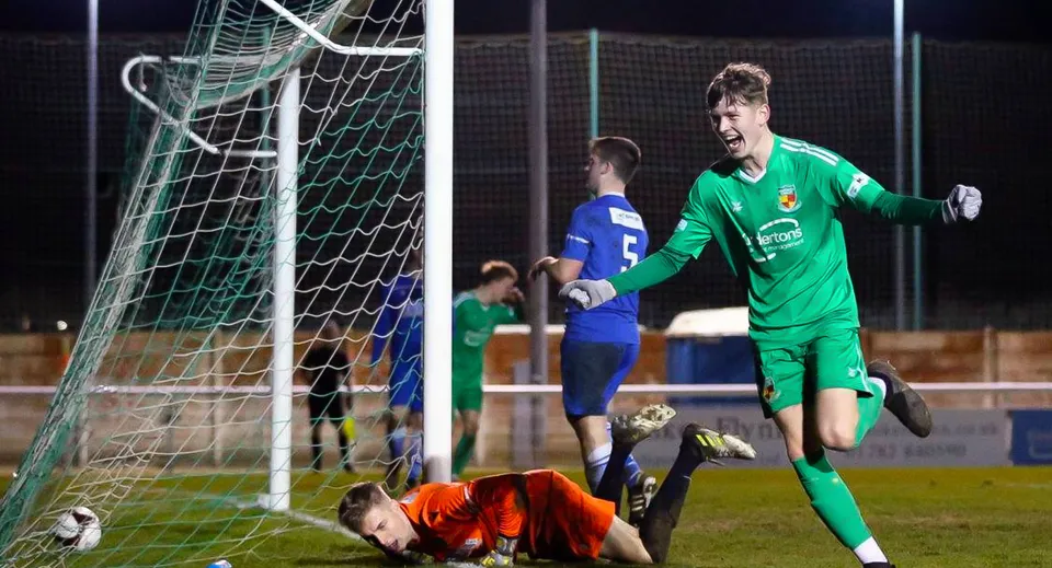 Un portiere in maglia verde fa una parata durante una partita di calcio sul campo sportivo del Cheshire College South & West.