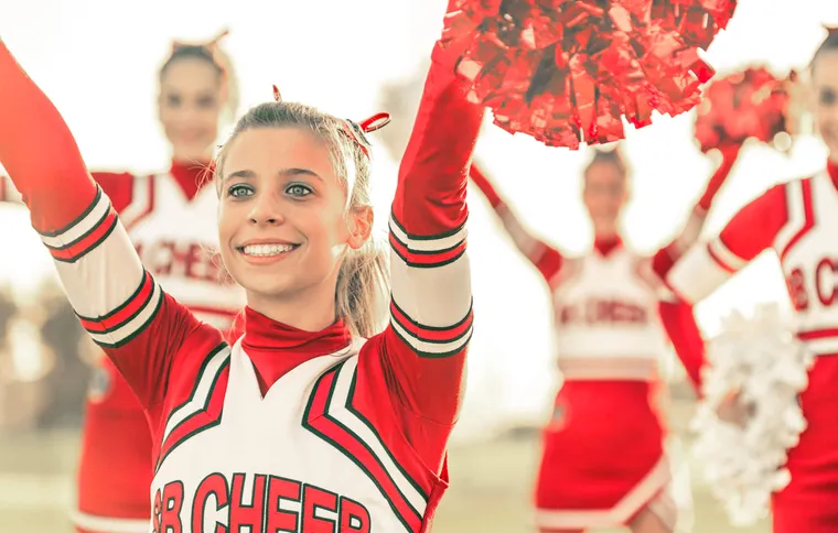 Lächelnde Cheerleaderin in rot-weißer Uniform hebt ihre Pompons