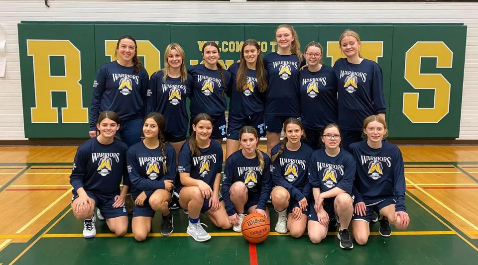 Un gruppo di giovani giocatrici di basket posa nella palestra della Tagwi Secondary School davanti al grande logo RAMS sulla parete.
