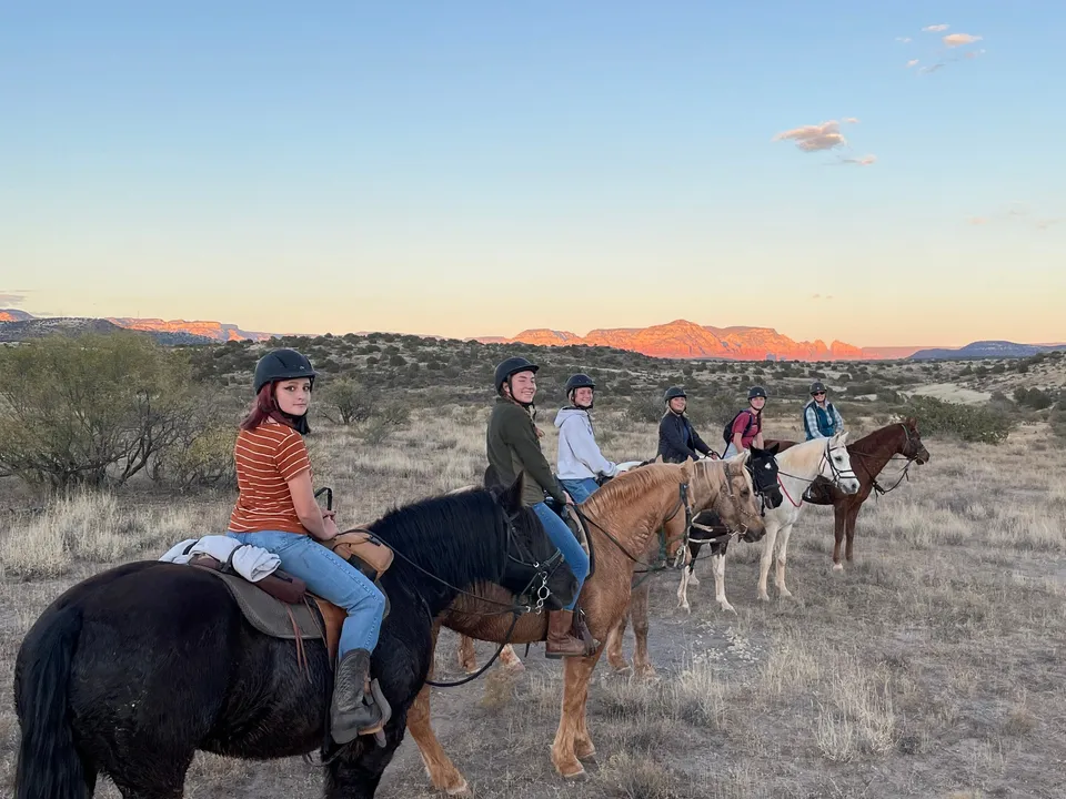 Studenti della Verde Valley School vanno a cavallo attraverso un paesaggio desertico suggestivo con montagne sullo sfondo.