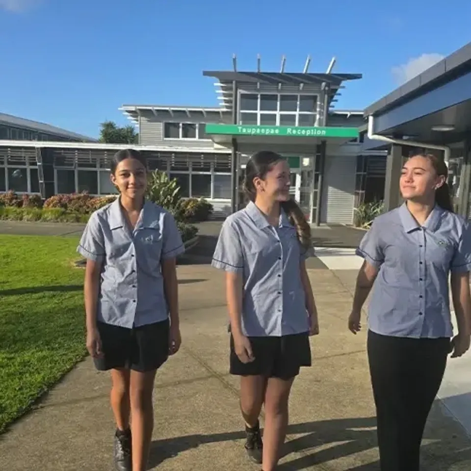 Tre studentesse in divisa grigia si trovano davanti a un edificio con un'insegna verde nel campus dello Spotswood College.