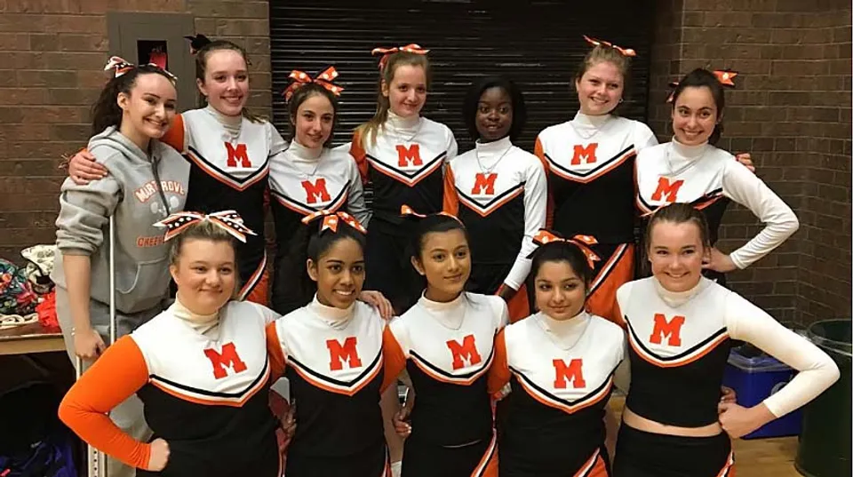 Un gruppo di giovani cheerleader in uniforme posa davanti a una parete in mattoni nel campus del Martingrove Collegiate Institute.