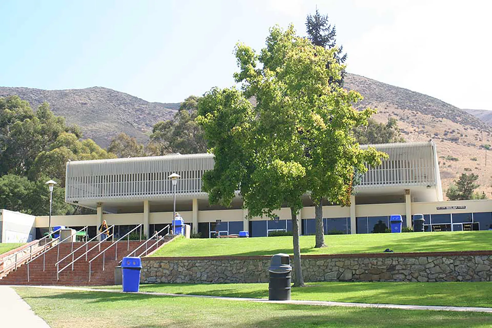 El moderno edificio de la San Luis Obispo High School con un césped y árboles en primer plano ante un fondo montañoso.