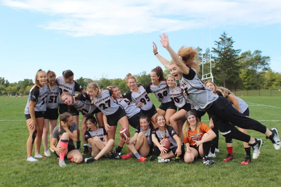 Un gruppo di giovani atlete della Orillia Secondary School si raduna su un campo sportivo con alberi sullo sfondo.