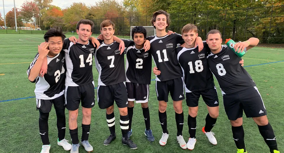 Un gruppo di giovani calciatori in maglia nera posa sul campo sportivo della H.J. Cambie Secondary School.